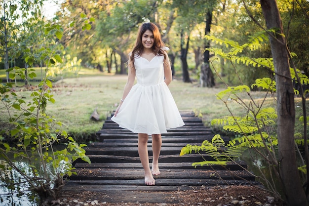 Menina bonita no vestido branco andar descalço na pequena ponte de madeira sobre a vala i