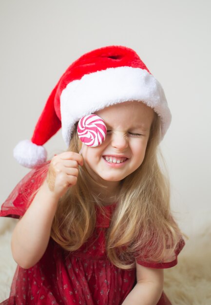 Menina bonita no vestido de festa vermelho de chapéu de Papai Noel esperando o Natal