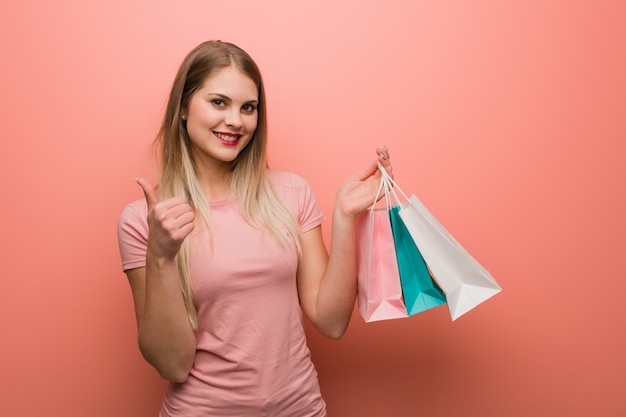 Menina bonita nova do russo que sorri e que levanta o polegar acima. ela está segurando uma sacola de compras.