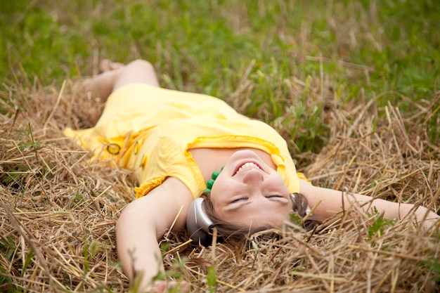 Menina bonita nova no amarelo com os fones de ouvido no campo.