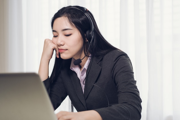 Menina bonita nova que trabalha em um portátil em uma empresa média pequena. Ela está operando os telefones e computador