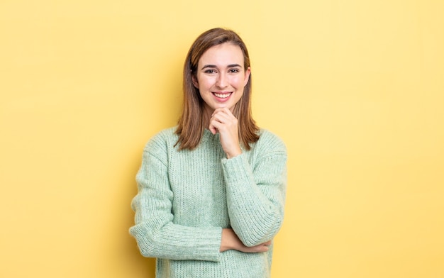 Menina bonita olhando feliz e sorrindo com a mão no queixo, imaginando ou fazendo uma pergunta, comparando opções