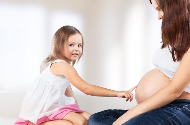 Menina bonita olhando para a barriga de grávida de sua mãe