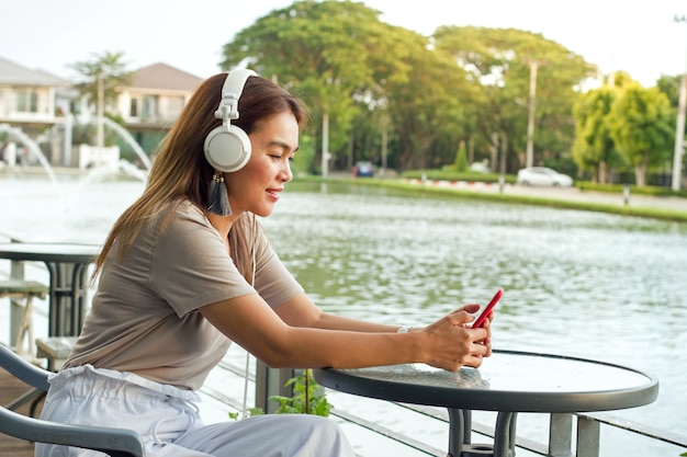 Menina bonita ouvir música com fones de ouvido brancos sentado no jardim com fundo de pântano