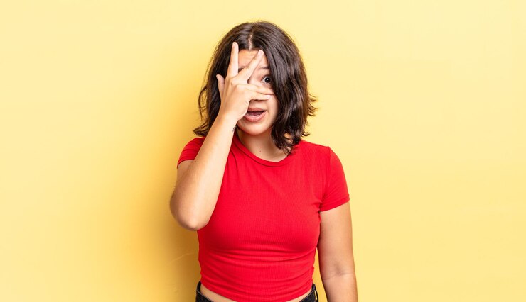 Foto menina bonita parecendo chocada, assustada ou apavorada, cobrindo o rosto com a mão e espiando por entre os dedos