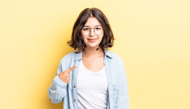 Menina bonita parecendo orgulhosa, confiante e feliz, sorrindo e apontando para si mesma ou fazendo o sinal número um