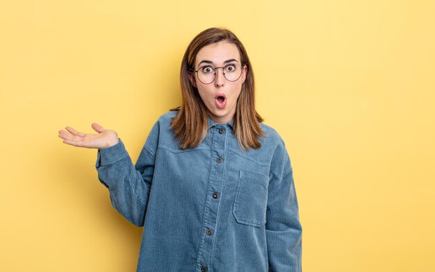 Menina bonita parecendo surpresa e chocada, com o queixo caído segurando um objeto com a mão aberta na lateral