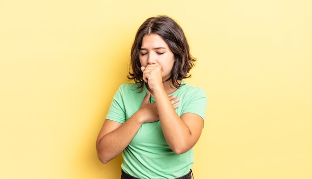 Menina bonita passando mal, com dor de garganta e sintomas de gripe, tosse com a boca coberta