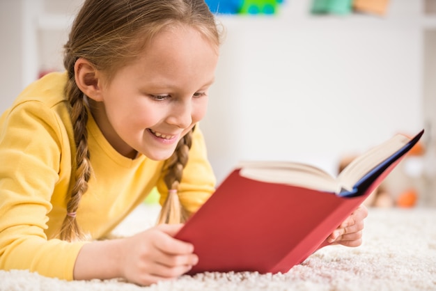 Menina bonita pequena no livro de leitura amarelo do pulôver.