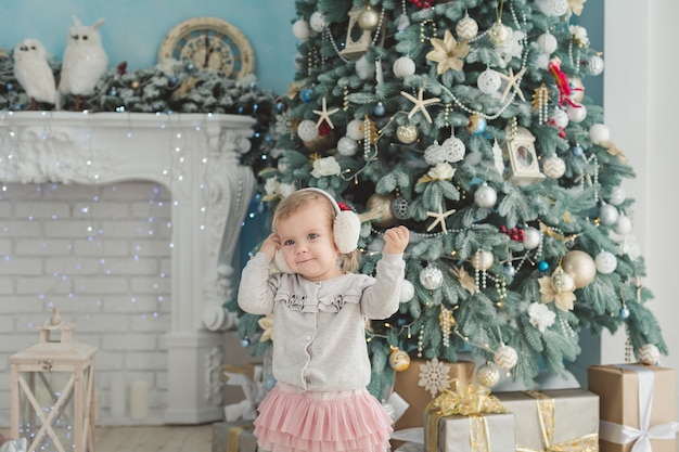 Menina bonita perto de árvore de Natal decorada com cavalo de balanço de madeira de brinquedo. Feliz Ano Novo. Retrato menina.