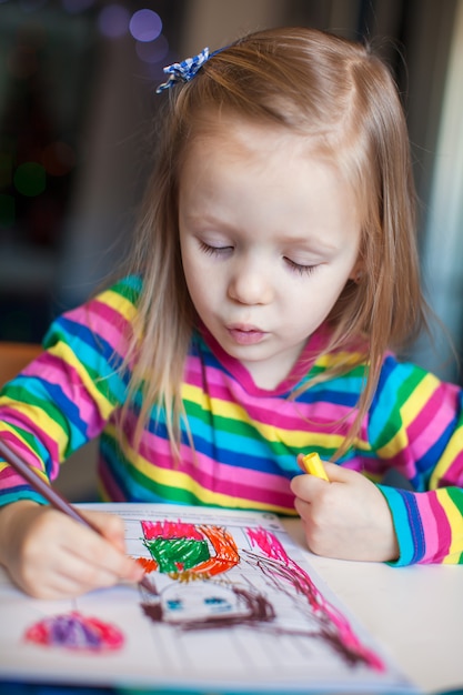 Menina bonita pintura com lápis enquanto está sentado na sua mesa