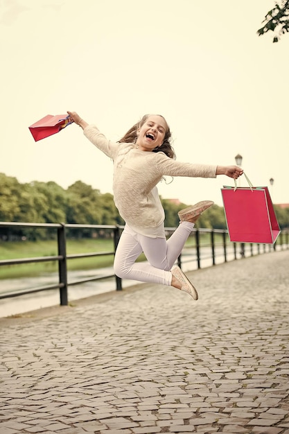 Menina bonita pulando na rua com sacolas de compras rosa