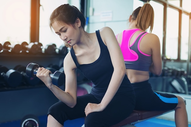 Menina bonita que exercita levantando um haltere para cuidados de saúde em um ginásio público