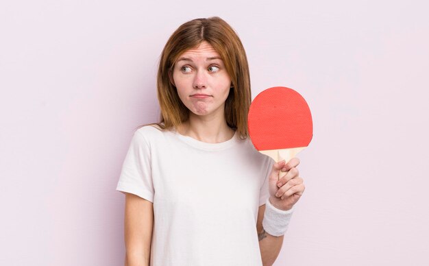 Menina bonita ruiva encolhendo os ombros sentindo-se confuso e incerto conceito de pingue-pongue