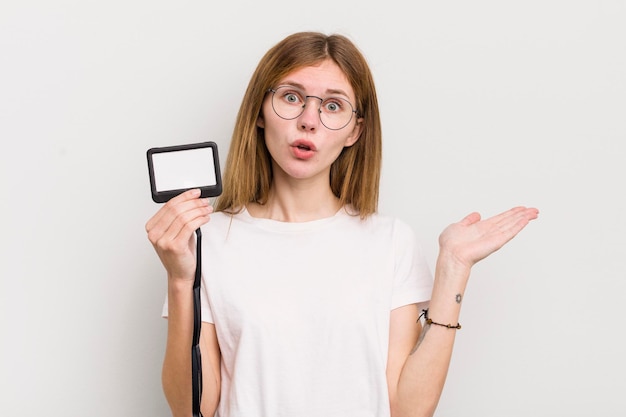 Menina bonita ruiva parecendo surpresa e chocada com o queixo caído segurando um conceito de identificação de passagem vip de objeto