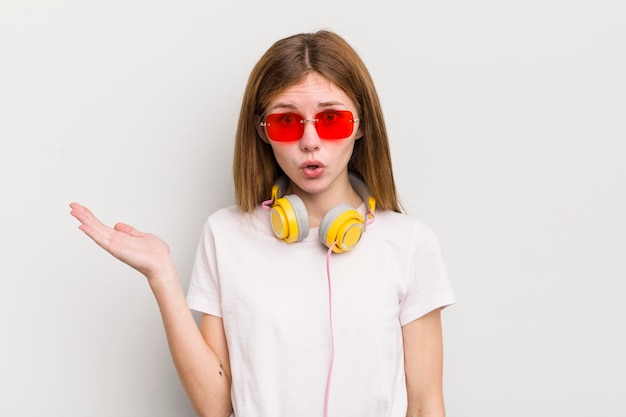 Menina bonita ruiva parecendo surpresa e chocada com o queixo caído segurando um objeto ouvir conceito de música