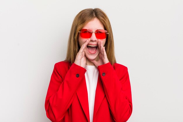 Menina bonita ruiva se sentindo feliz dando um grande grito com as mãos ao lado da boca