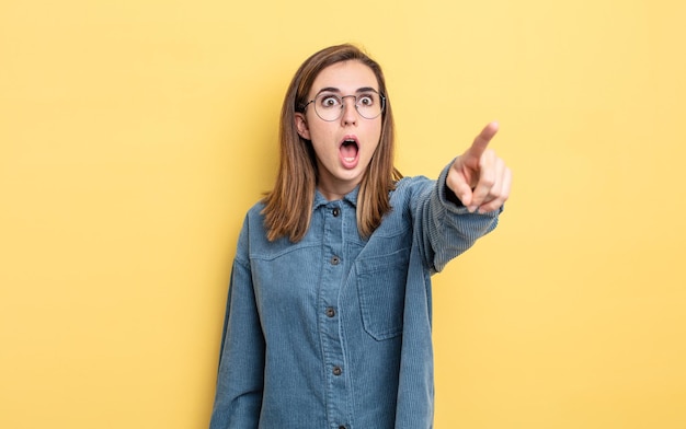 Menina bonita se sentindo chocada e surpresa, apontando e olhando para cima com admiração e expressão boquiaberta