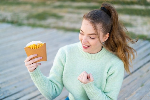 Menina bonita segurando batatas fritas ao ar livre comemorando uma vitória