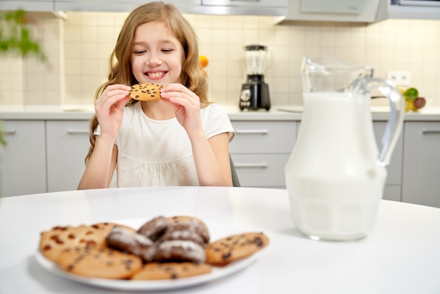 Menina bonita sentada à mesa, comendo biscoitos com passas.