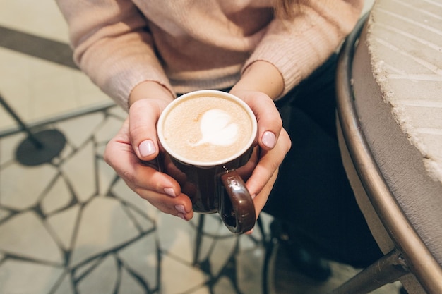 Menina bonita sentada com uma xícara de café em um café Mulheres adoráveis gosta de café em uma cafeteria Xícara de café nas mãos femininas