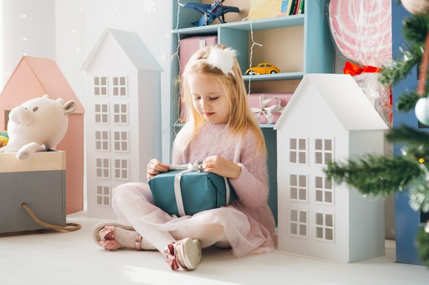 Menina bonita sentada na árvore de Natal segurando uma caixa com um presente