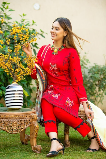 Menina bonita sentada na cadeira no jardim usando vestido vermelho moderno Desi