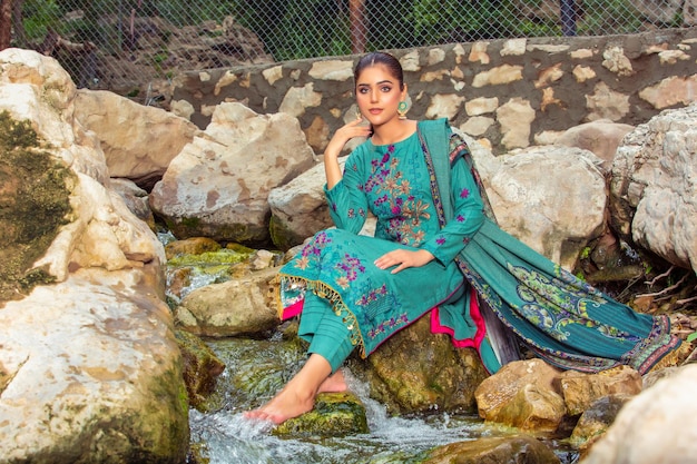 Menina bonita sentada nas rochas no parque temático para ensaio de moda usando vestido tradicional Desi