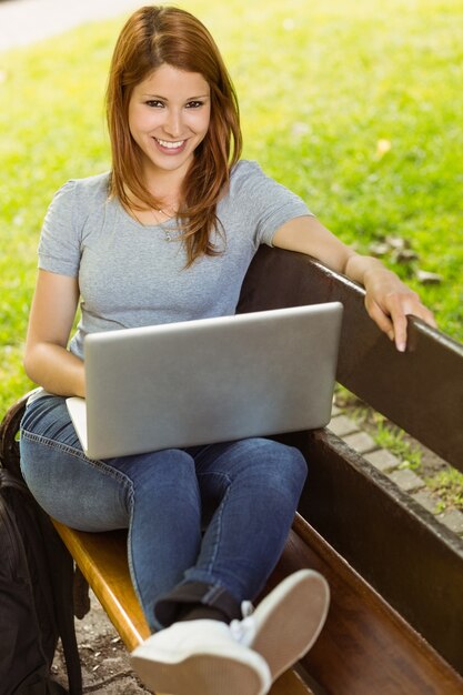 Menina bonita sentada no banco usando o laptop sorrindo para a câmera