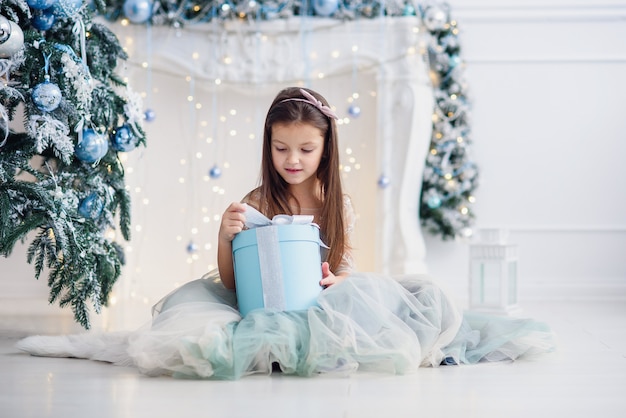 Menina bonita sentada perto de árvore de Natal dentro de casa.