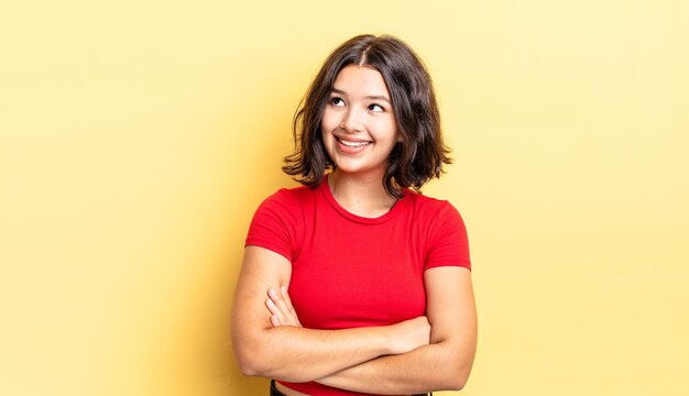 Menina bonita sentindo-se feliz, orgulhosa e esperançosa, imaginando ou pensando, olhando para cima para copiar o espaço com os braços cruzados