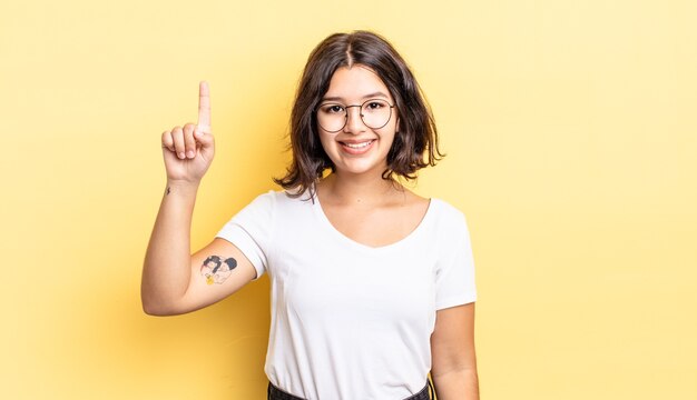 Menina bonita sorrindo alegre e feliz, apontando para cima com uma mão para copiar o espaço