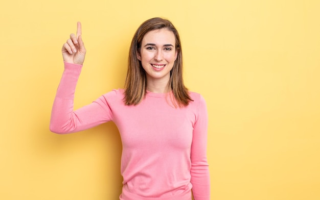 Menina bonita sorrindo alegre e feliz, apontando para cima com uma mão para copiar o espaço