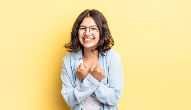 Menina bonita sorrindo alegremente e comemorando, com os punhos cerrados e os braços cruzados, sentindo-se feliz e positiva