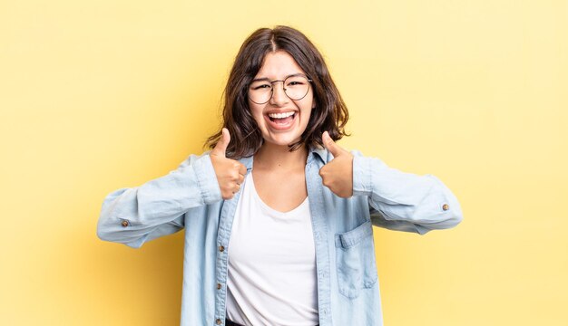 Menina bonita sorrindo amplamente feliz, positiva, confiante e bem sucedida, com os dois polegares para cima