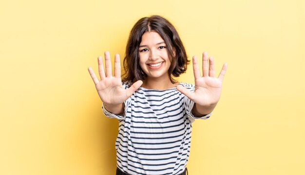 Menina bonita sorrindo e parecendo amigável, mostrando o número dez ou décimo com a mão para a frente, em contagem regressiva