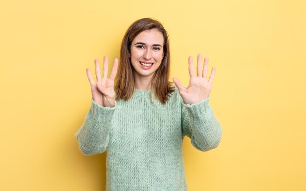 Menina bonita sorrindo e parecendo amigável, mostrando o número nove ou nono com a mão para a frente, em contagem regressiva