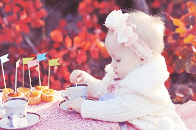 Menina bonita usa vestido de princesa tomando chá com decoração ao ar livre