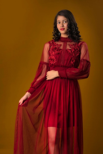 Menina bonita usando um lindo vestido vermelho posando em fundo marrom