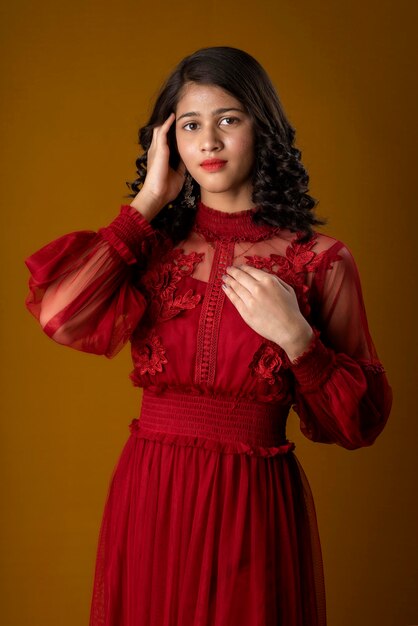 Menina bonita usando um lindo vestido vermelho posando em fundo marrom