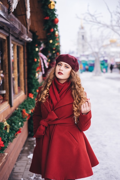 Menina bonita, vestindo um casaco vermelho e uma boina na rua de Natal