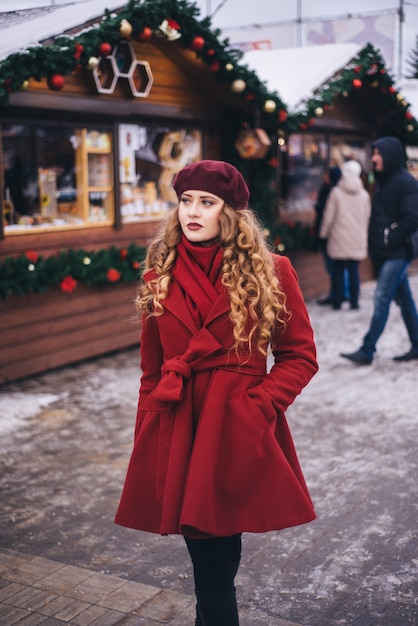 Menina bonita, vestindo um casaco vermelho e uma boina na rua de Natal