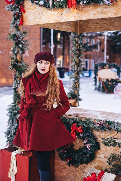 Menina bonita, vestindo um casaco vermelho e uma boina na rua de Natal