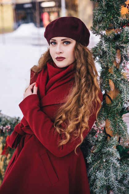 Menina bonita, vestindo um casaco vermelho e uma boina na rua de Natal