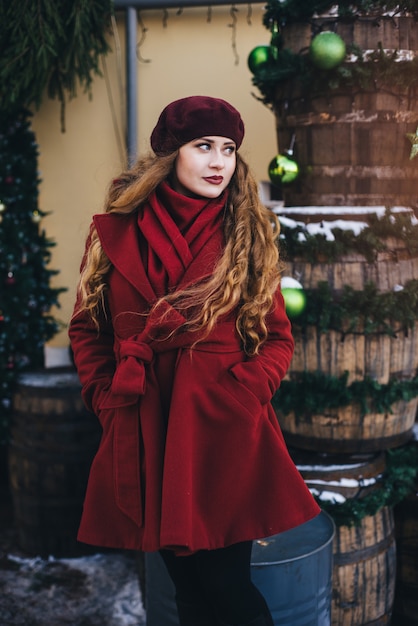 Menina bonita, vestindo um casaco vermelho e uma boina na rua de Natal