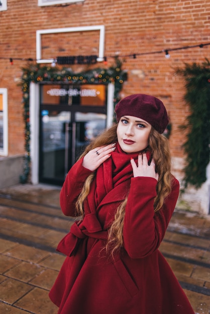 Menina bonita, vestindo um casaco vermelho e uma boina na rua de Natal