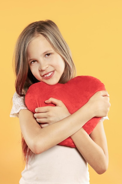 Menina bonitinha abraça o coração de brinquedo vermelho grande com força
