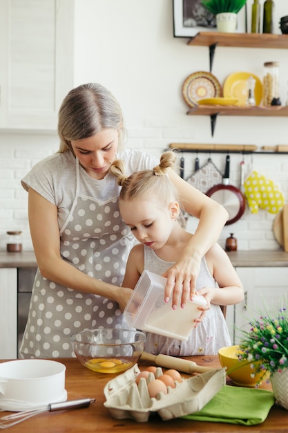 Menina bonitinha ajuda a mãe a assar biscoitos na cozinha. Família feliz. Toning.