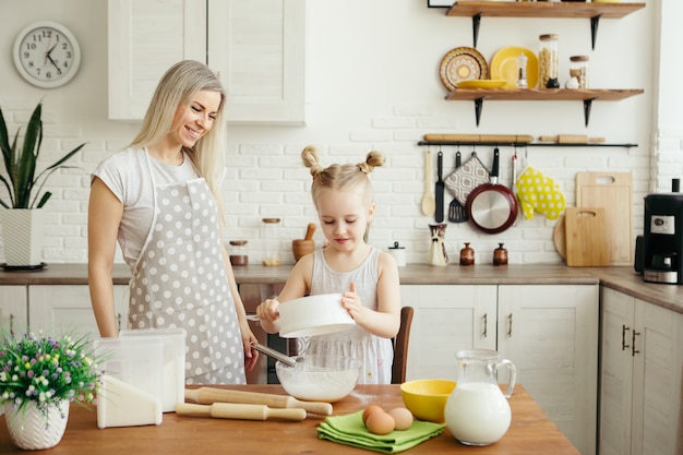 Menina bonitinha ajuda a mãe a assar biscoitos na cozinha. Família feliz. Toning.