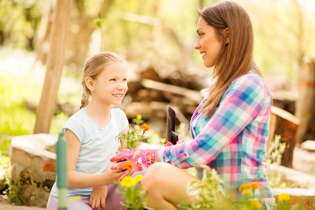 Menina bonitinha ajudando a mãe plantando flores em um quintal.